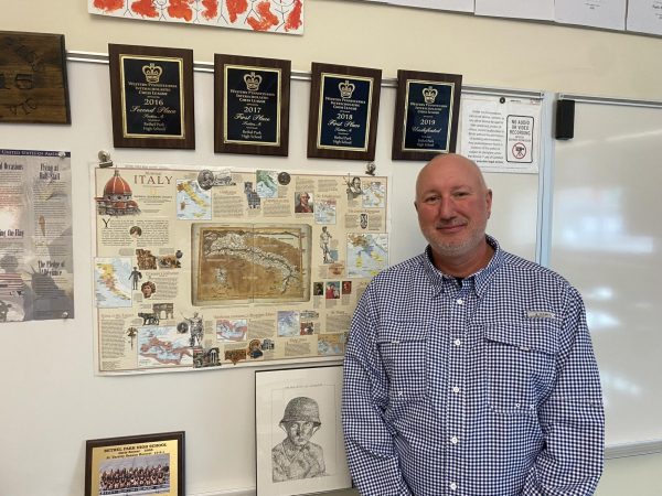 Mr. Vic, Chess Club sponsor, poses in front of various award plaques the Chess Club has earned over the years under his direction.