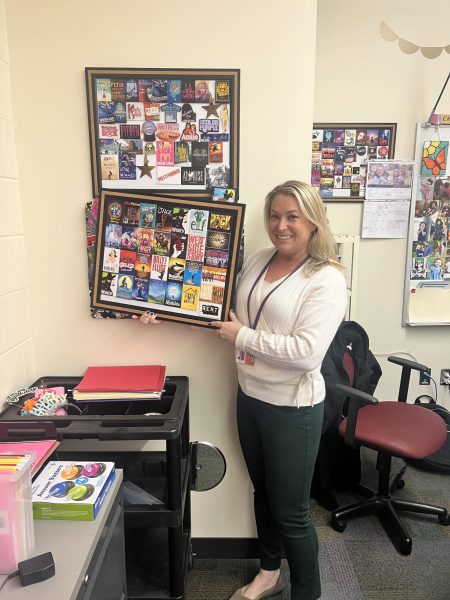 Mrs. Chapin proudly poses with her various Broadway musical ticket stubs she has on display in her office.