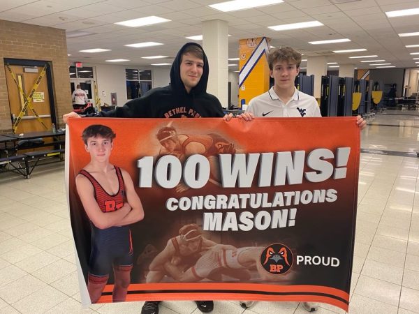 Mason Kernan, alongside his brother Hunter, proudly holds his 100 wins banner after achieving a milestone in his wrestling career.